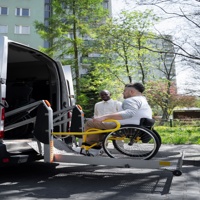 Wheelchair user boarding an accessible van using a lift with assistance from a support worker