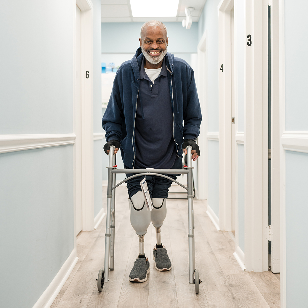 smiling man with prosthetic legs practices walking with walker at floyd brace