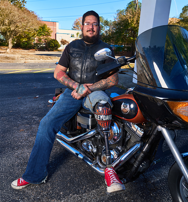 man sits on motorcycle showing off custom prosthetic leg with Harley Davidson design
