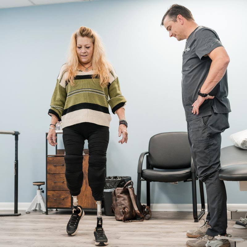 smiling man with prosthetic legs practices walking with walker at floyd brace