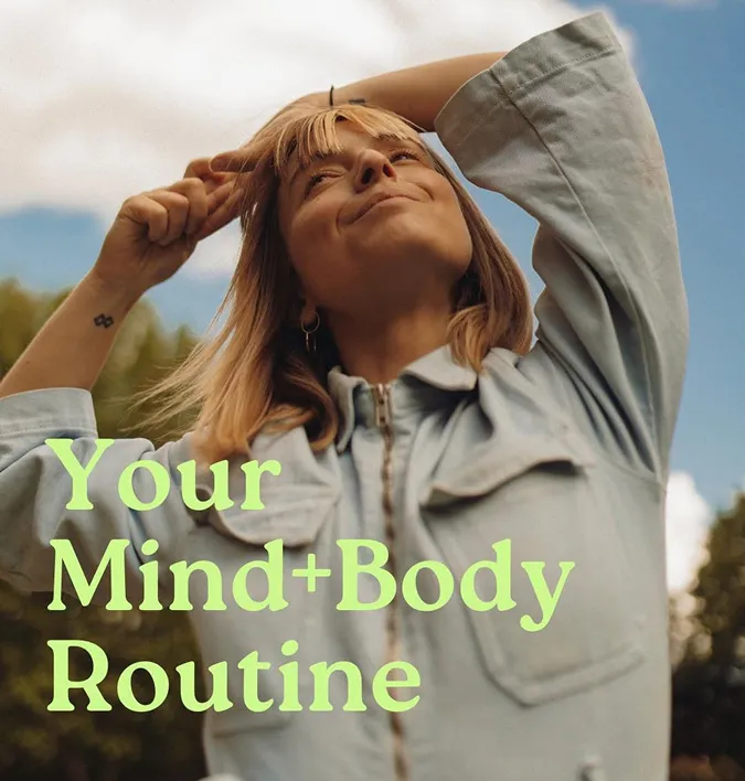 Smiling woman outdoors wearing a light denim jacket, joyfully pointing at her head with eyes closed, symbolizing balance and positivity. Overlay text reads: “Your Mind + Body Routine.”
