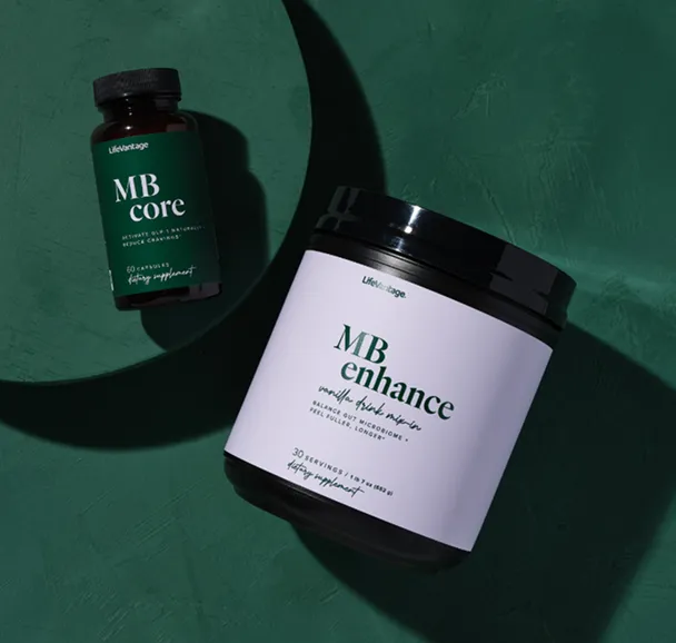 Flat lay photo of two LifeVantage supplement containers on a dark green surface. One is a small bottle labeled “MB Core” containing 60 capsules, and the other is a larger container labeled “MB Enhance,” a vanilla-flavored metabolic health drink mix with 30 servings.