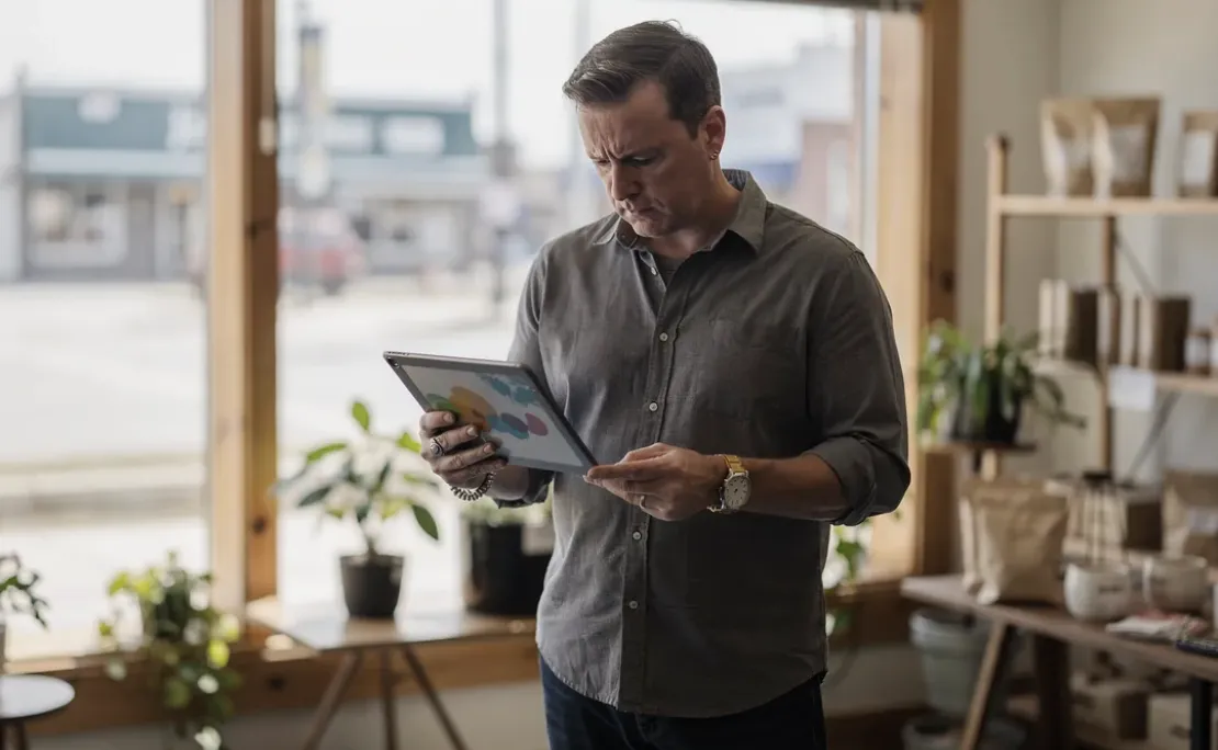 Muskegon business owner reviewing digital advertising results on a tablet inside a local storefront.