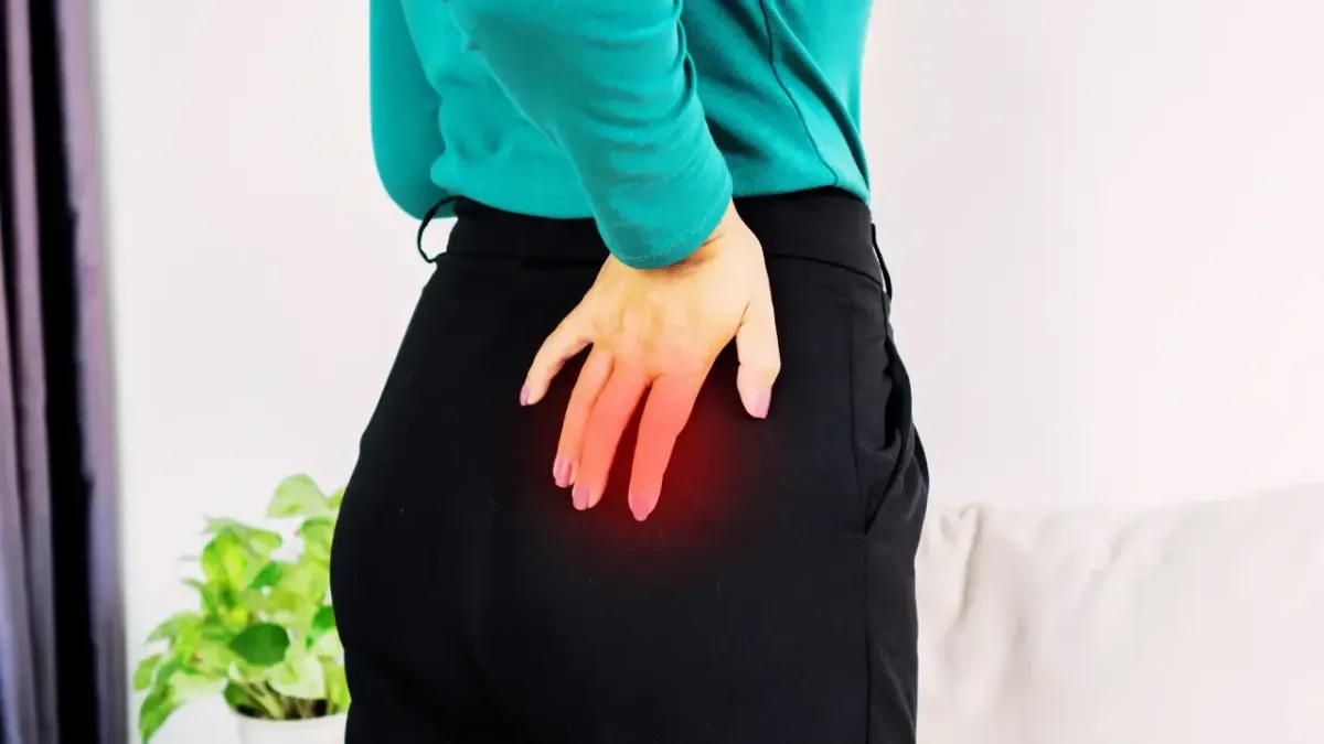 A woman clutching her lower back and glute muscle in discomfort, with a red glow overlay illustrating radiating sciatica pain from a herniated disc in Fort Mill, SC.