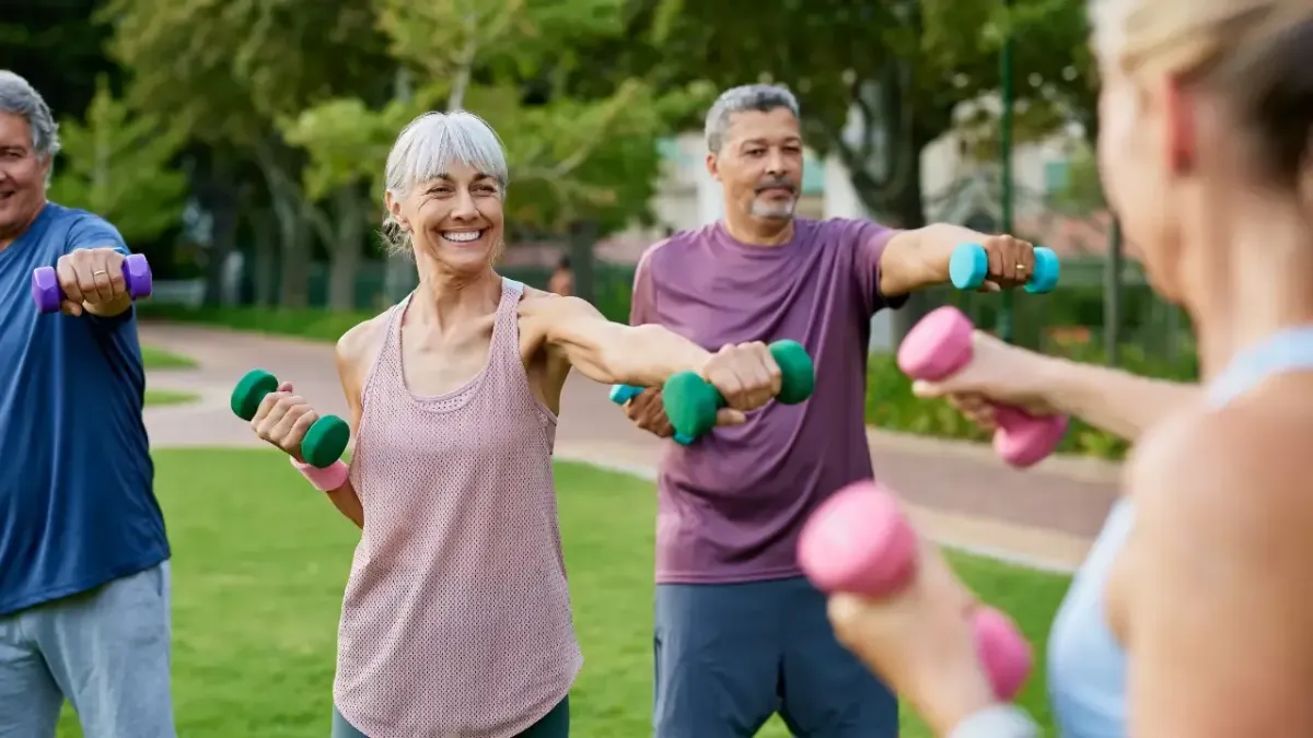 A group of active senior adults exercising with light dumbbells in a park to build core stability and prevent lower back pain under the guidance of a Fort Mill chiropractor.