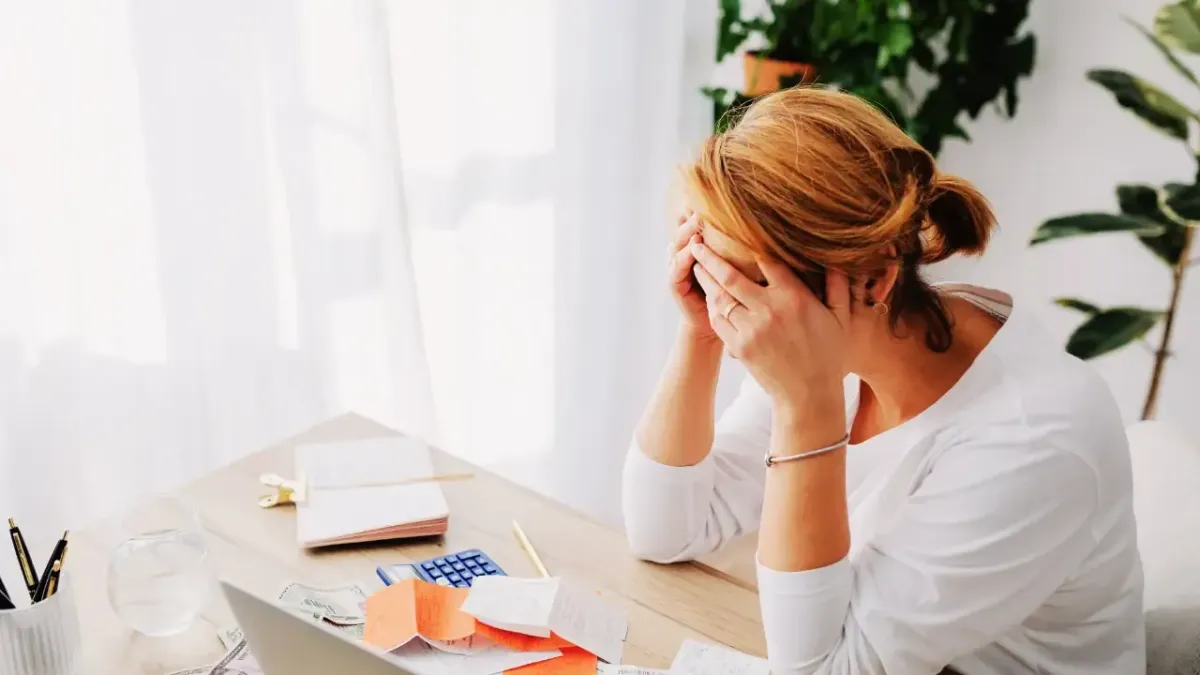 A woman sitting at her desk holding her head in distress due to a severe migraine, illustrating stress and posture triggers managed with headache treatment in Fort Mill, SC.