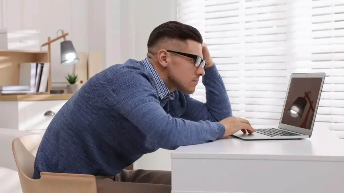 A man slouching forward with poor ergonomics while typing on a laptop at his desk, demonstrating workspace posture habits that aggravate shoulder stiffness in Fort Mill, SC.