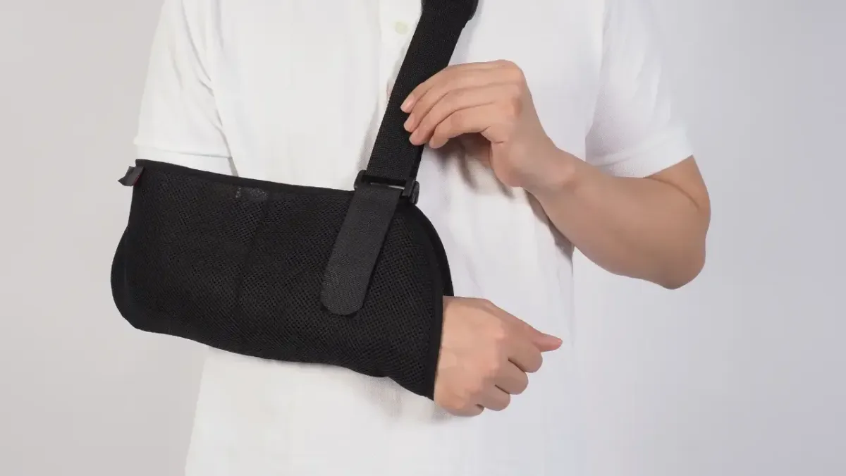 A man in a white polo shirt wearing a black mesh supportive arm sling to immobilize his shoulder joint during injury recovery in Fort Mill, SC.