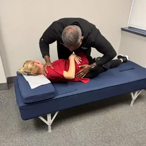 A back pain specialist performing a side-posture manual lumbar spine adjustment on a patient at Gonstead Chiropractic Center in Fort Mill, SC.