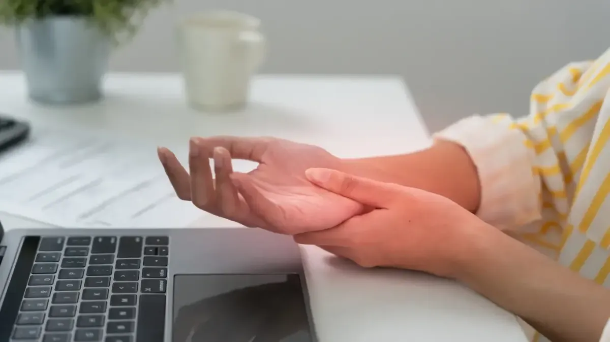 An office worker massaging their painful wrist and palm next to a laptop, seeking natural carpal tunnel relief in Fort Mill SC.