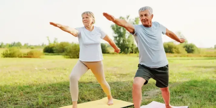Senior man and woman practicing Warrior II yoga pose outdoors after chiropractic care in Gonstead Chiropractic Center in Fort Mill SC