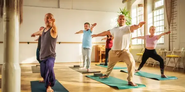 Group of adults holding Warrior II pose in a bright studio