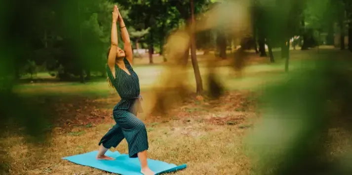 Woman holding Warrior I pose on blue mat outdoors in park