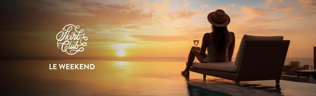 Le Weekend 2026 banner image with woman sitting in a lounge chair on a beach with a wine glass watching the sunset.