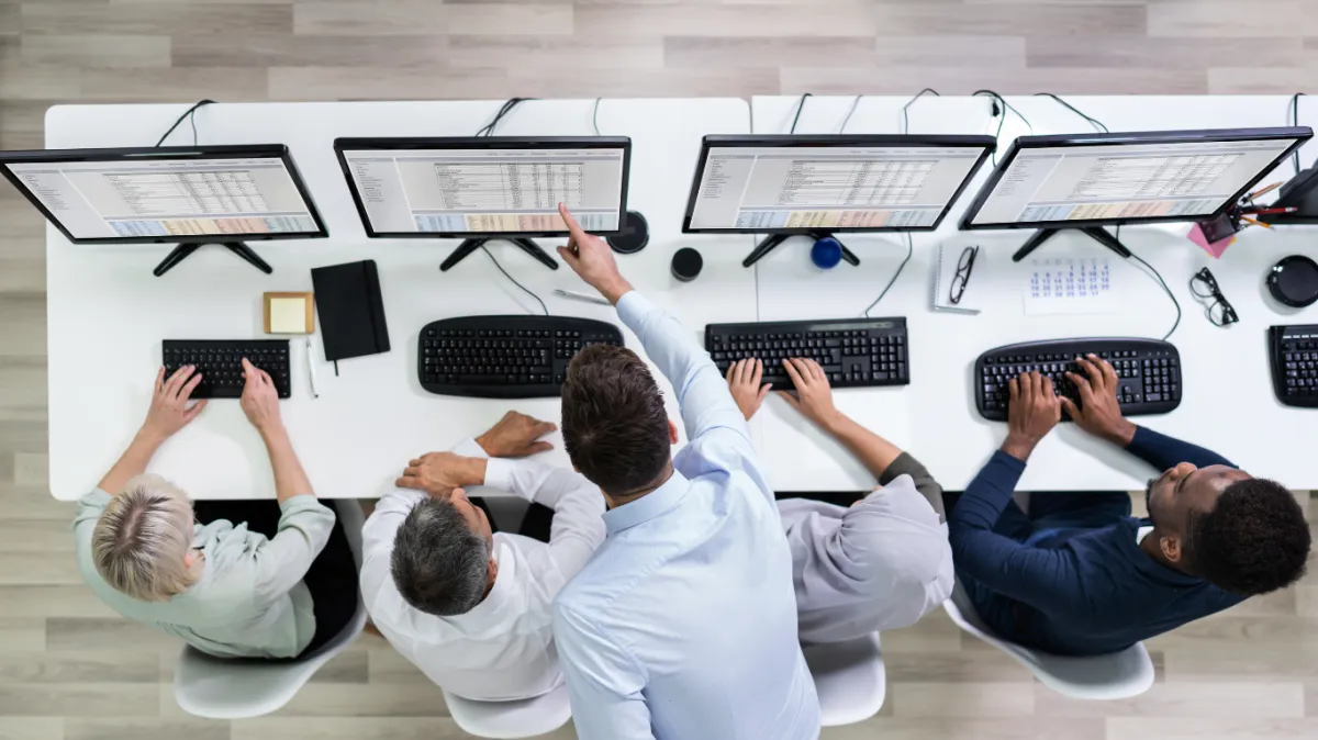 top down shot of 5 people working in front of a computer with one of them teaching the other one
