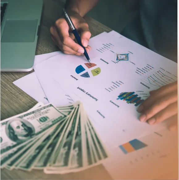 close up shot of a person's hand and a document with graphs in numbers and a fanned out money on the side