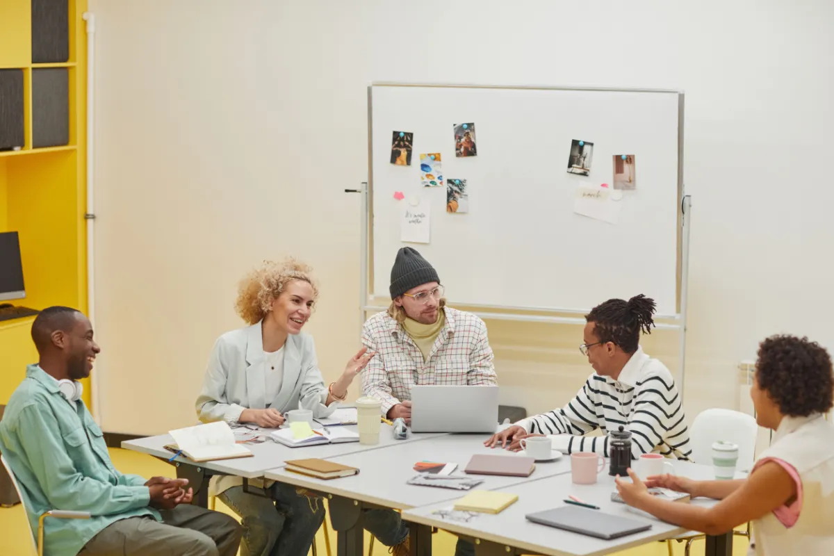 Small team gathered around a table with laptops and notes, collaborating on real workplace challenges, reflecting the programme’s focus on tools built around actual decisions and responsibilities.