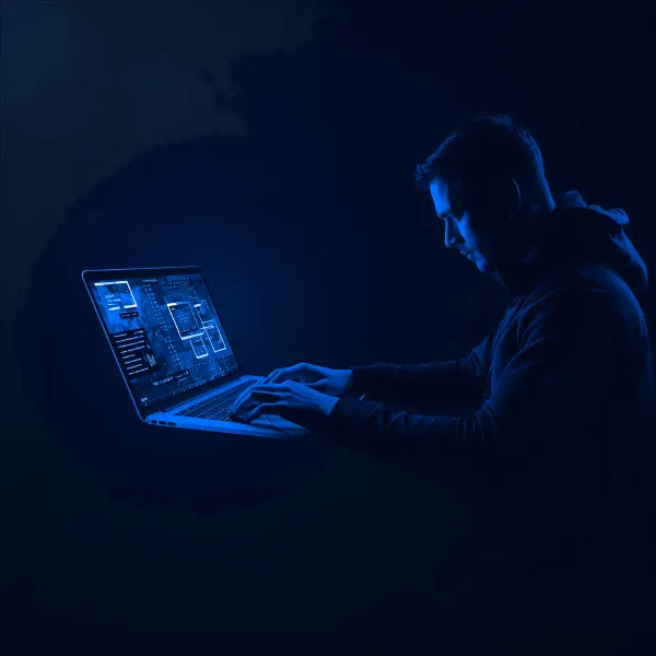 A man illuminated by purple light types on a laptop displaying futuristic digital interfaces and data visualizations against a dark background.