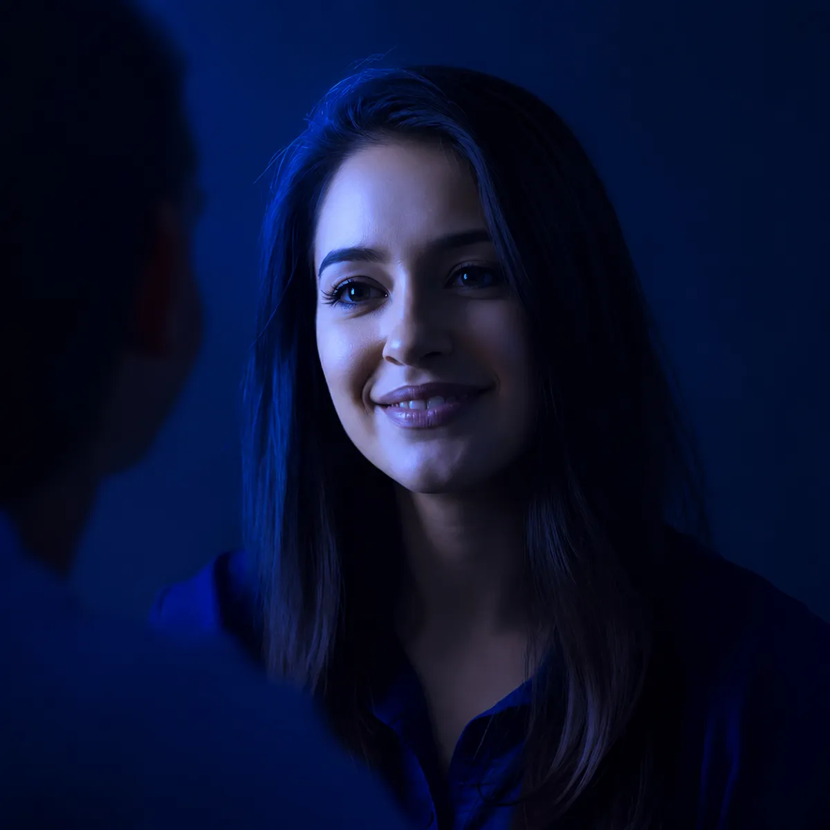 Woman smiling warmly while talking to someone, lit with soft purple lighting.