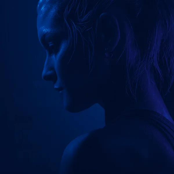 Profile of a female athlete covered in sweat, lit dramatically with blue and purple lighting against a dark background.