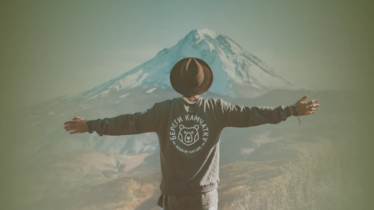 Man standing with arms open in front of a mountain, symbolizing strength, confidence, and personal growth.