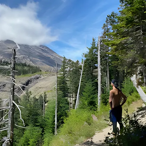 Man standing shirtless on a mountain trail, reflecting on personal struggles and the journey of self-discovery.