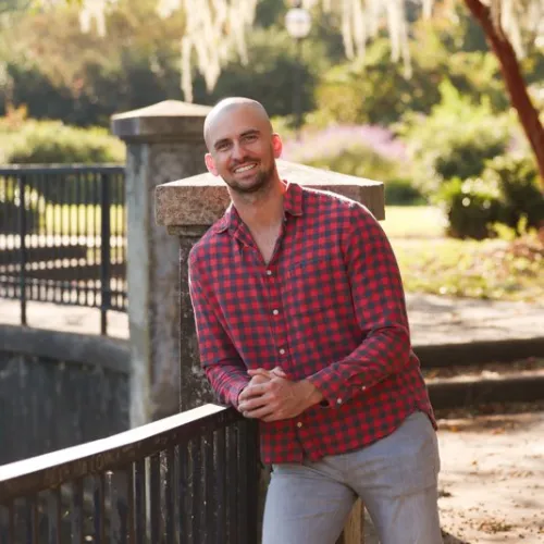 Anthony Speeney smiling near a railing, symbolizing empowerment, mental health mastery, and personal growth.