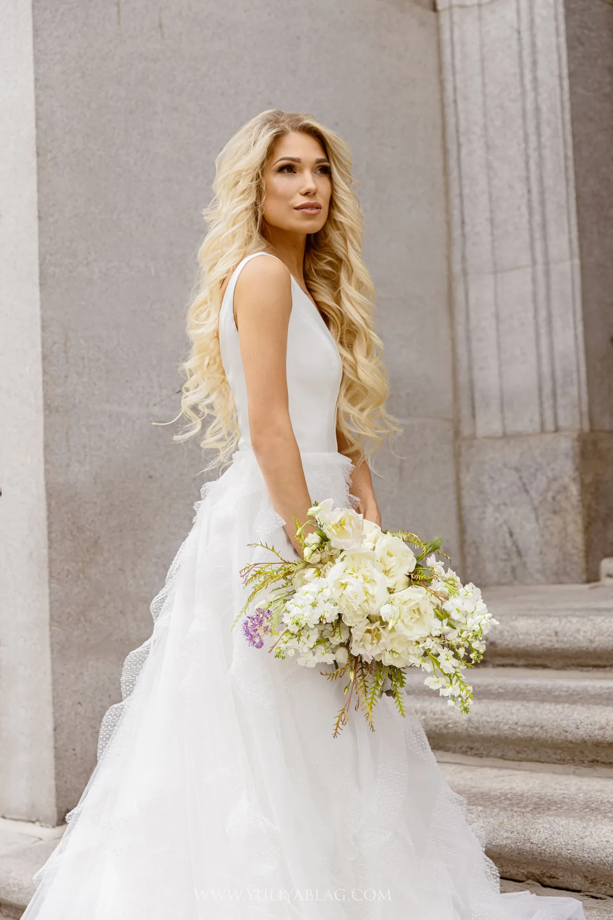 Mariée en robe à col en V tenant un bouquet champêtre blanc