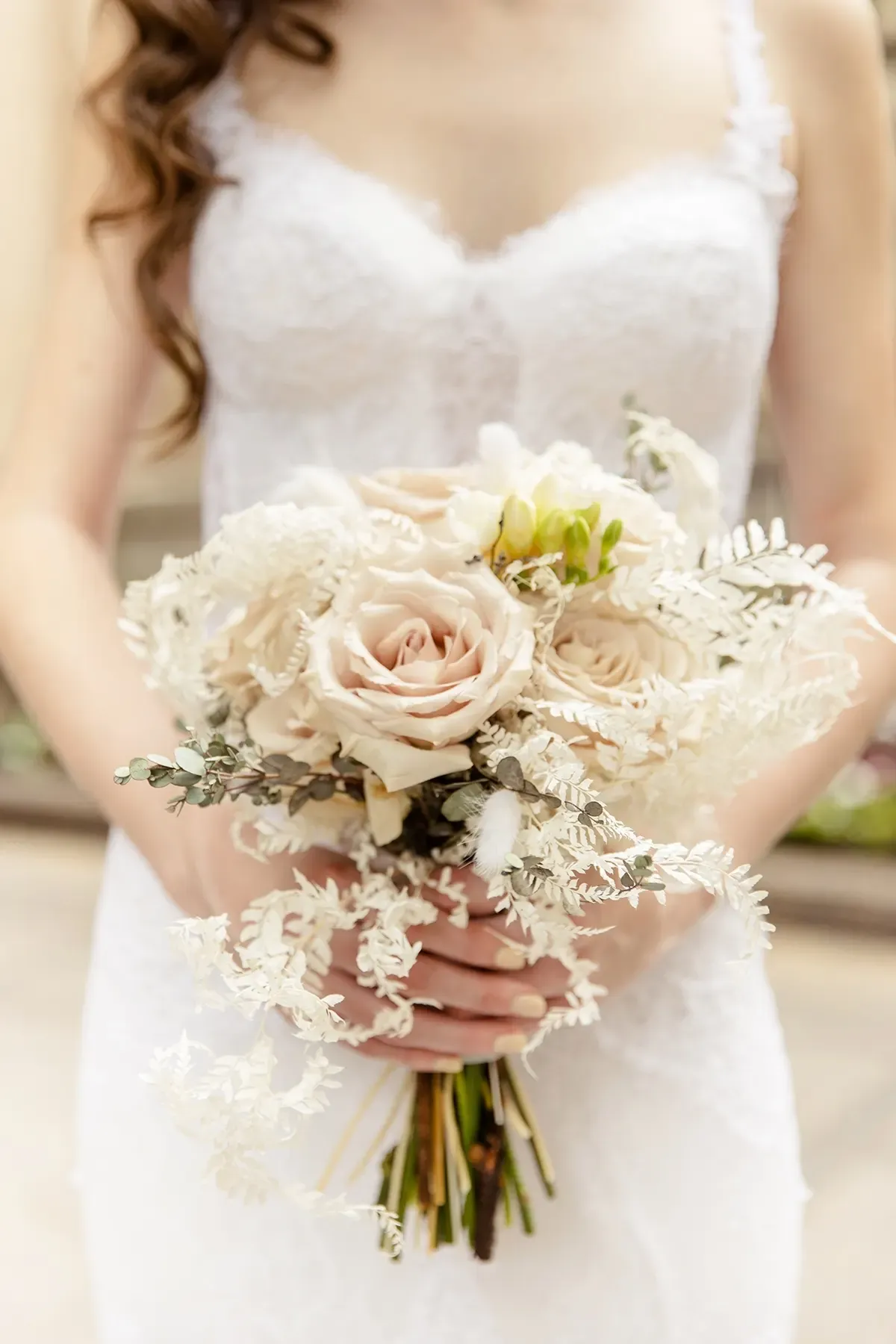 Bouquet de mariée de roses poudrées et de fleurs séchées contre une robe de dentelle