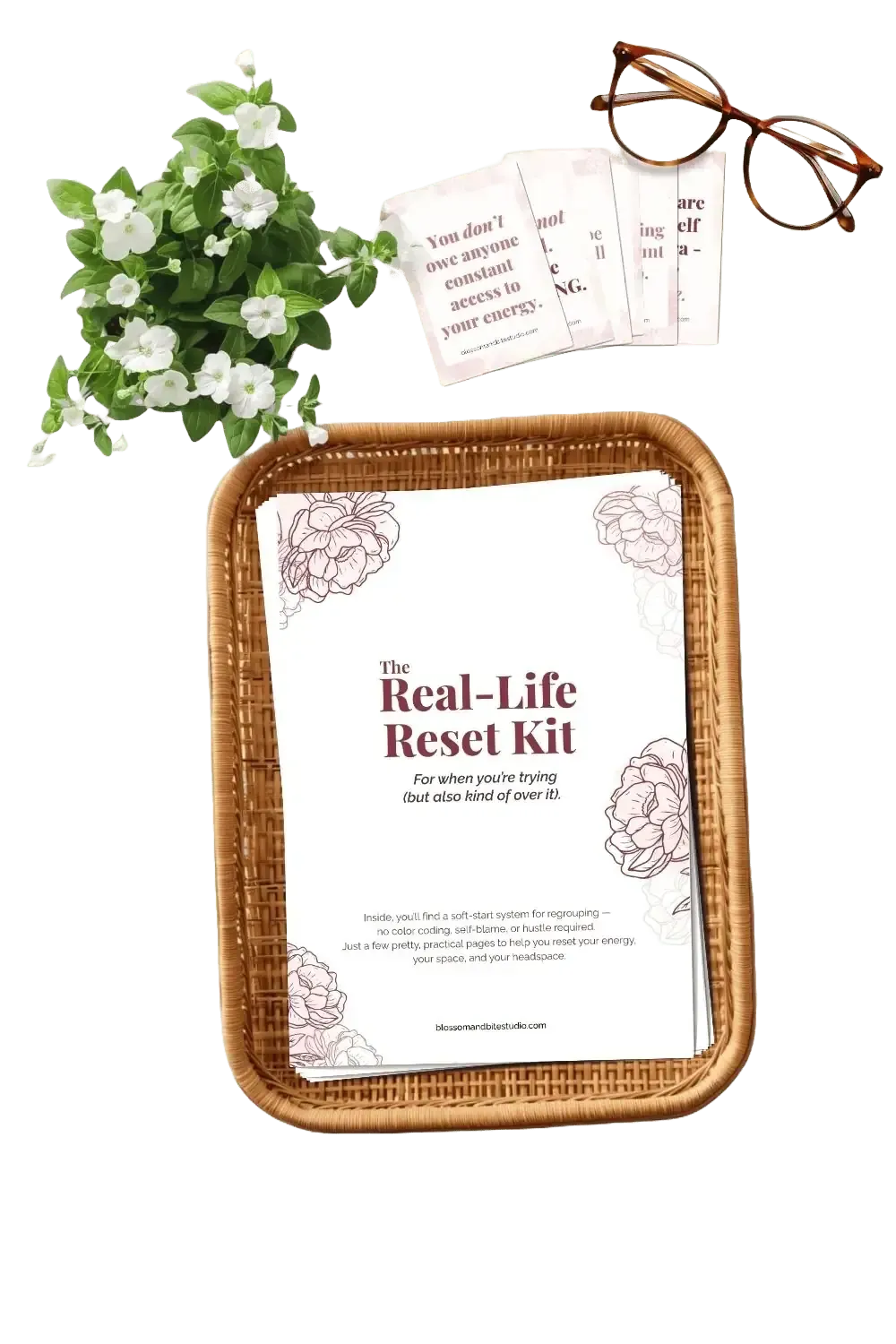 Printed copy of The Real-Life Reset Kit in a rattan tray with white flowers and tortoiseshell glasses on a soft pink background.