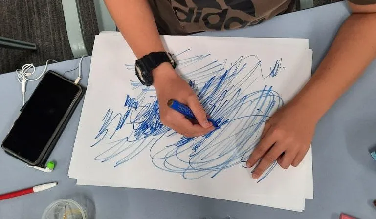 A close-up of a child’s hands creating expressive blue scribbles on a piece of paper during an in-person workshop for Arthritis NSW (Charity) in Sydney, Australia.