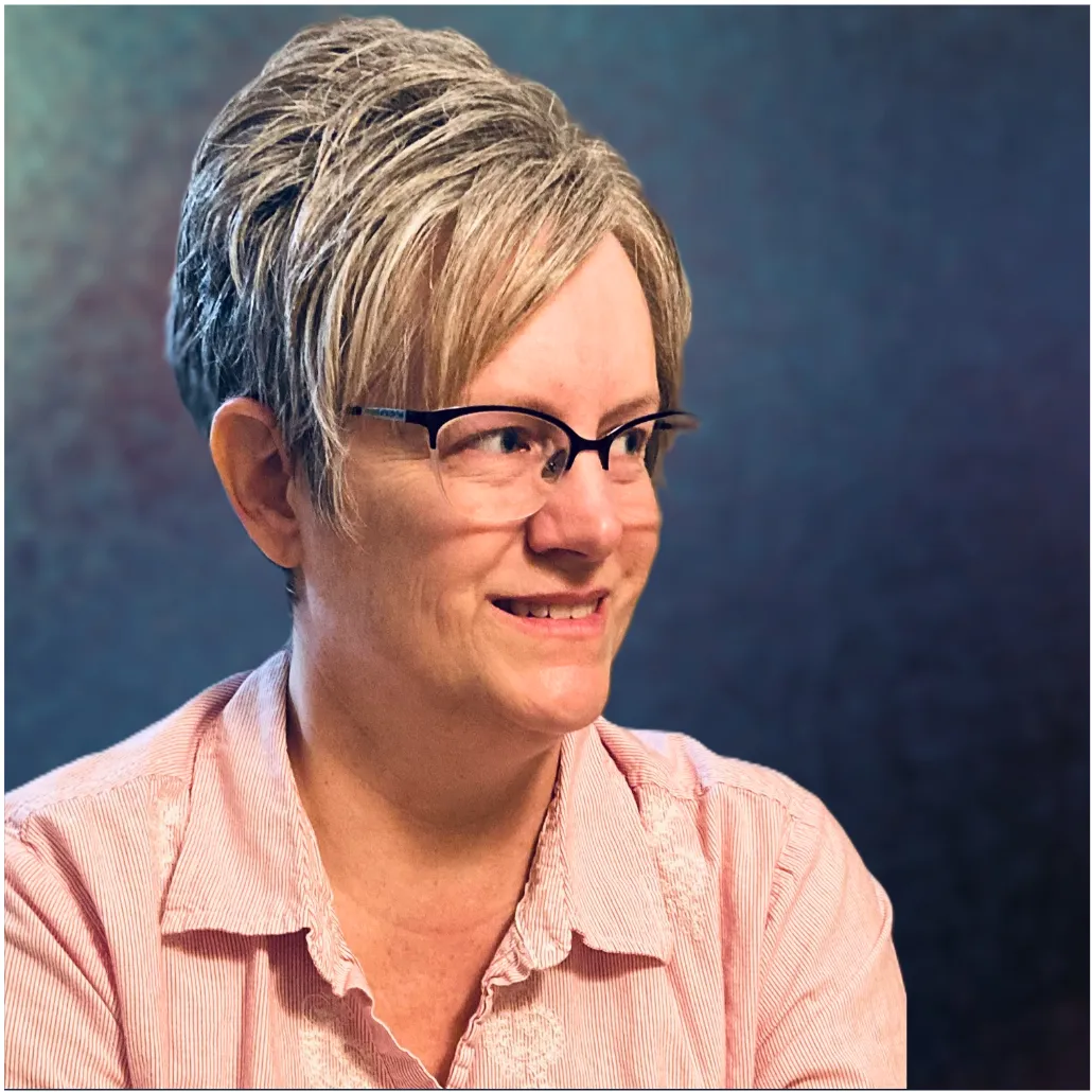 Image of a woman with short gray hair. She is wearing a pink blouse and eyeglasses 