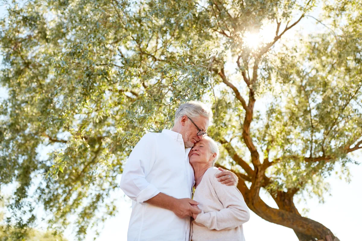 Loving, retired married couple, hugging under a big tree on a sunny day in Provo, Utah