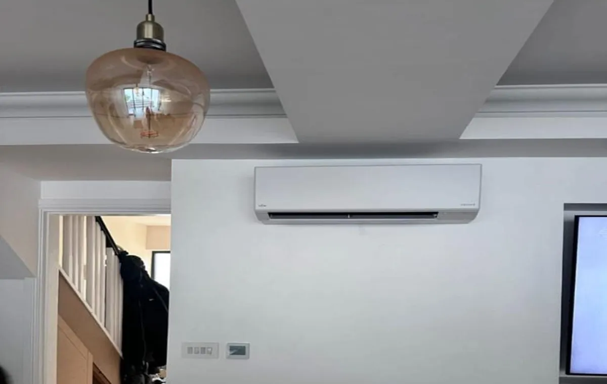 A modern room with a white wall features a mounted air conditioner. A spherical glass pendant light hangs from the ceiling, adding a sleek, minimalistic touch.