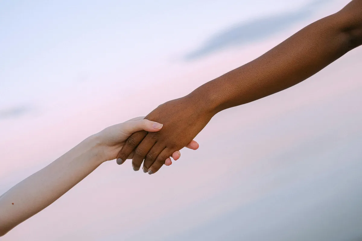 Interracial hands holding against a pastel sky background, representing unity, diversity, and human connection.