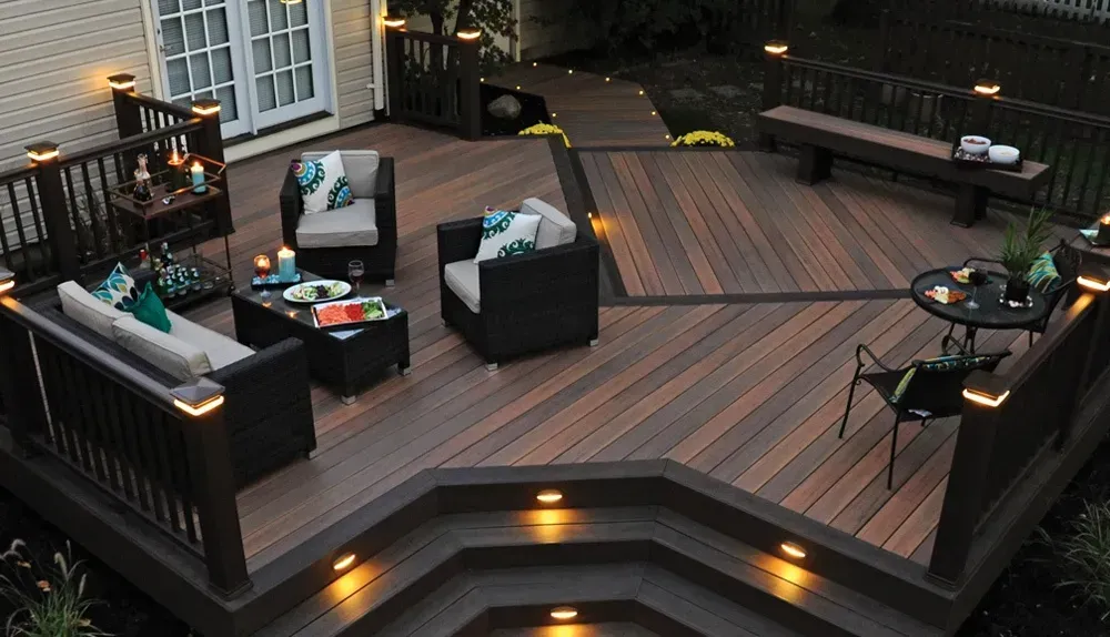 A multi-level deck at dusk with two-toned wood, multiple seating areas, and built-in lights on the steps and railings.