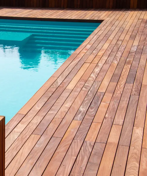 A newly installed wooden deck runs alongside a swimming pool with clear blue water.