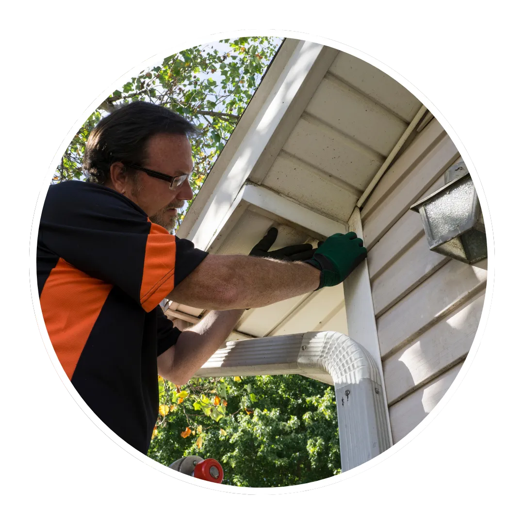 A person with glasses and a black and orange shirt is shown from the chest up, working on a white gutter system.