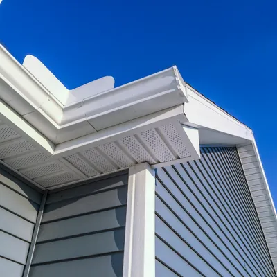 Corner of a house with blue siding and white trim against a blue sky.