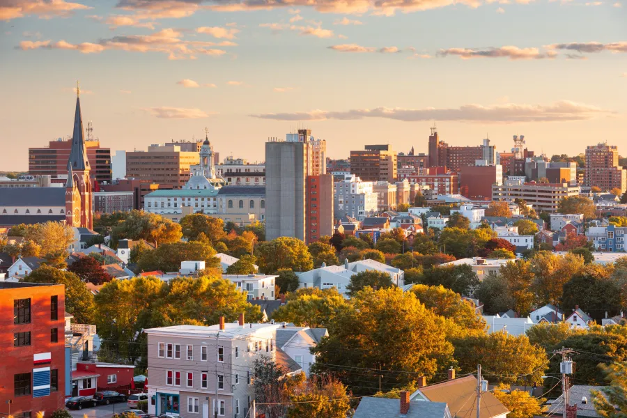 Urban skyline with residential homes, trees, and buildings during sunset with warm lighting.