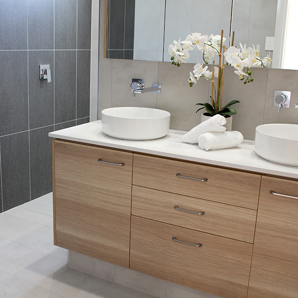 Modern bathroom vanity with double sinks, wood cabinets, and orchid decor in a clean minimalist space.