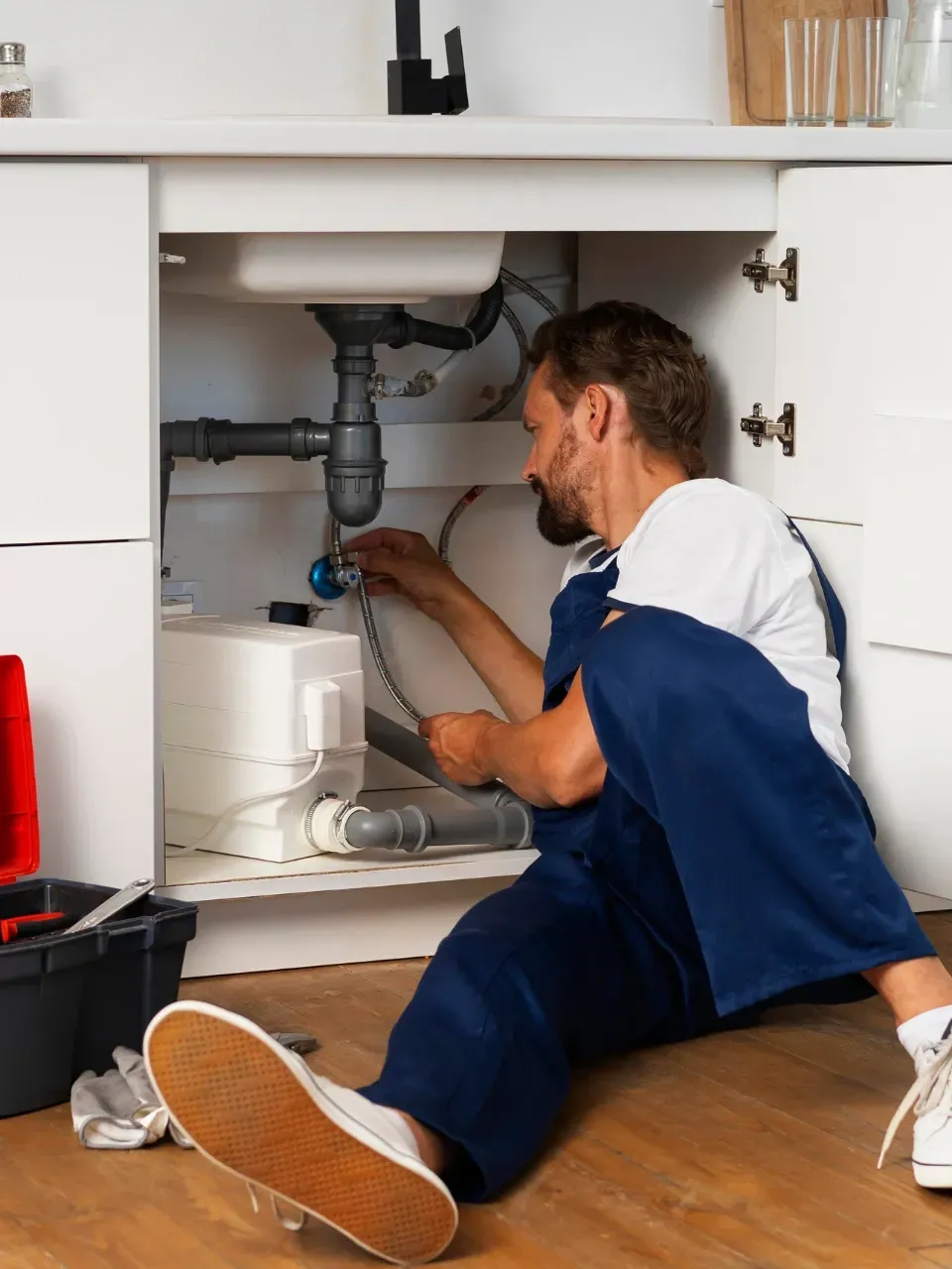Tradesman working under a sink with tools, unable to answer phone