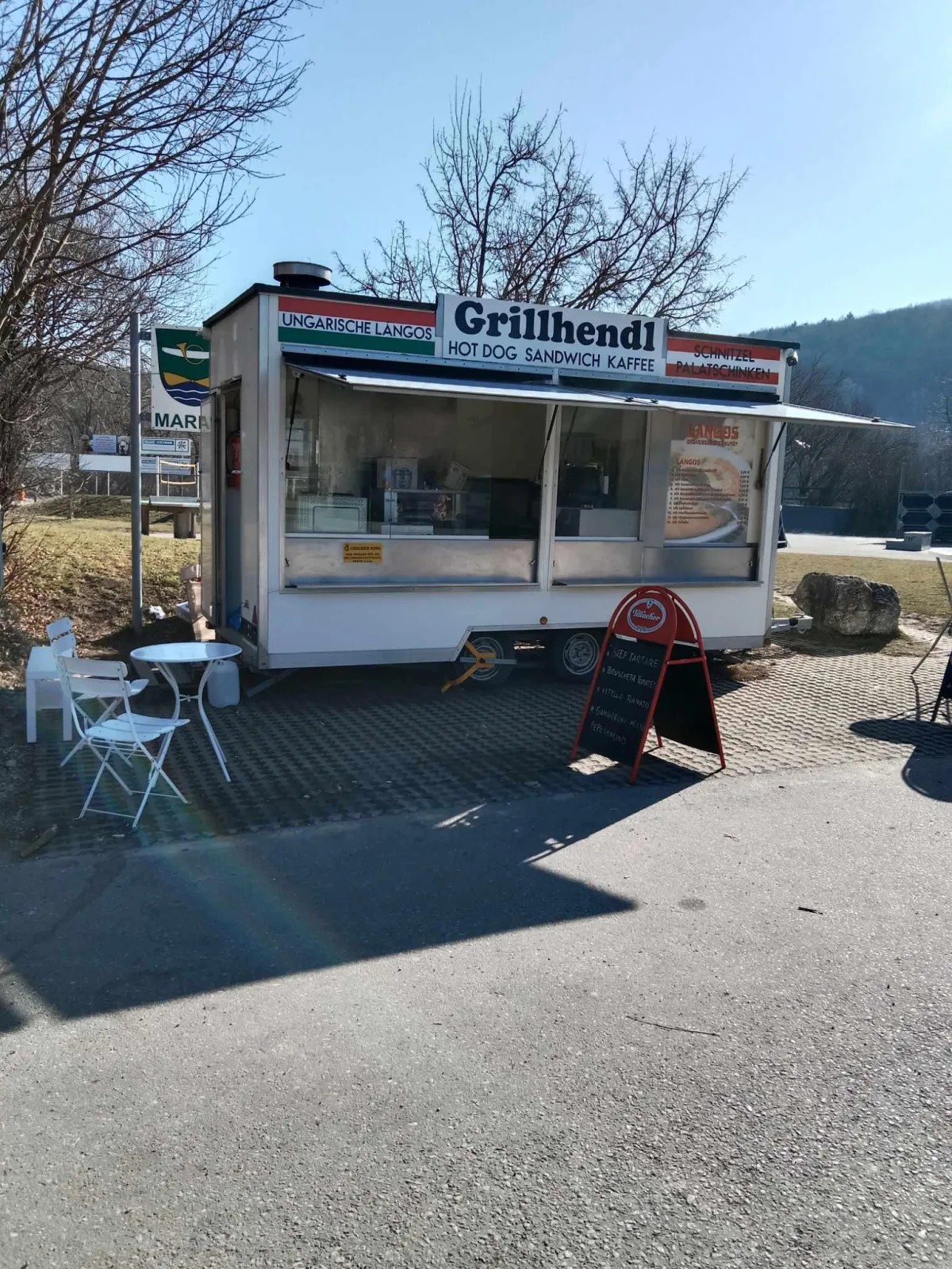 Nahaufnahme eines Grillhähnchens am Spieß im Freien, knusprige Haut, goldbraune Farbe, warmer Tageslichtschein.