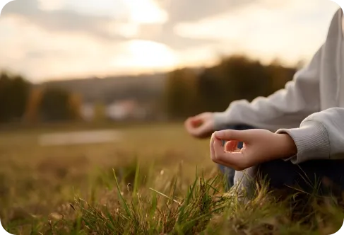 A person sitting cross-legged on grass outdoors, possibly meditating, illuminated by sunlight