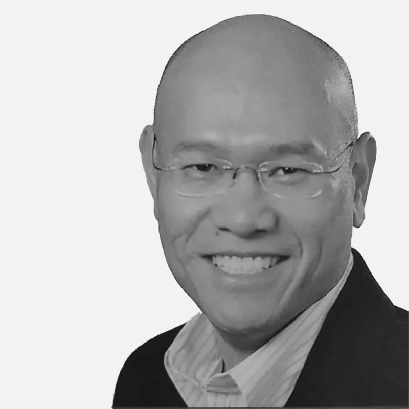 Black and white portrait of a smiling Asian man wearing glasses and a suit, cropped in a square