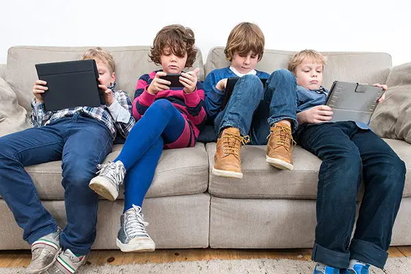 Four children comfortably seated on a couch, each using a tablet, illustrating a scene of modern leisure and technology use.