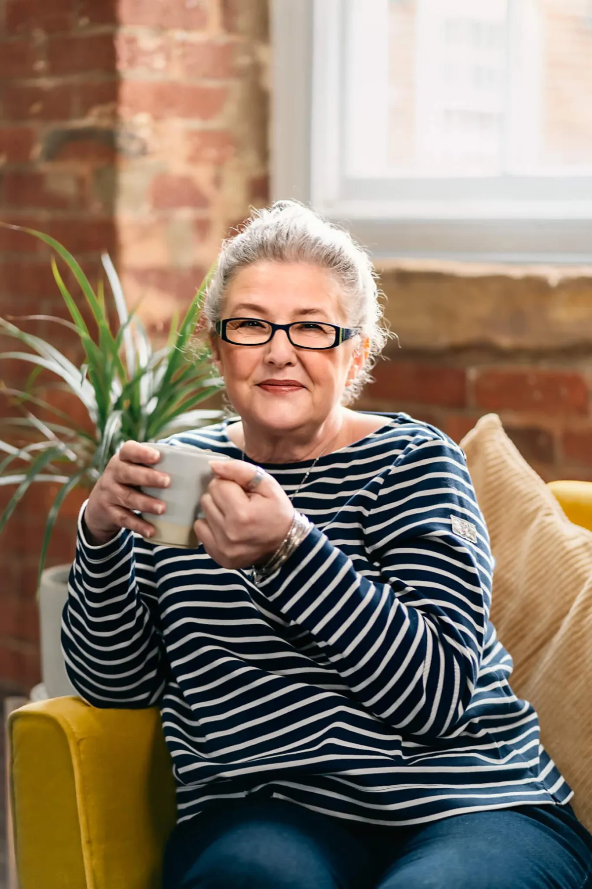 Nancy Detchon sat on a sofa having a cup of coffee, smiling.