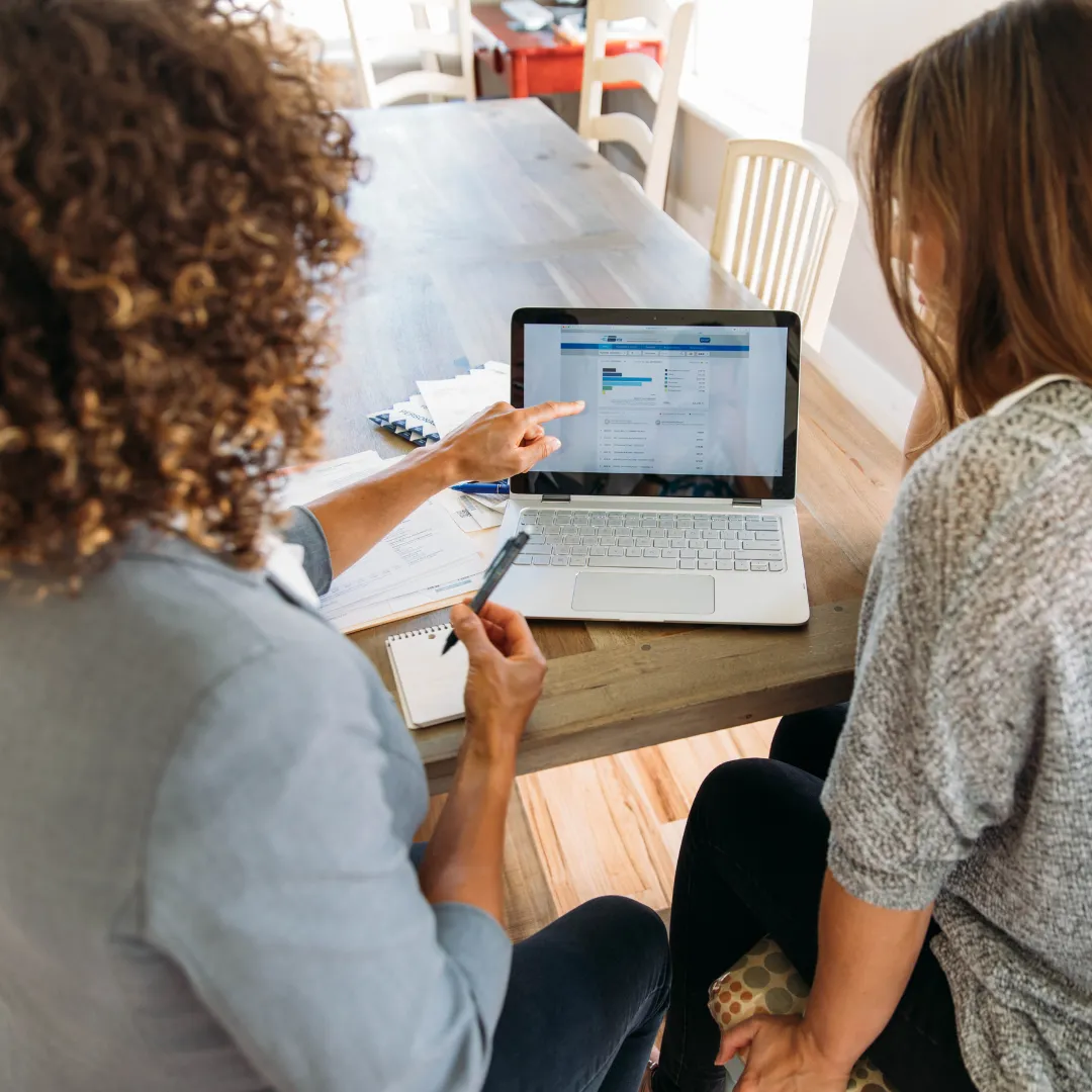 Two women sitting together and looking at figures on a laptop