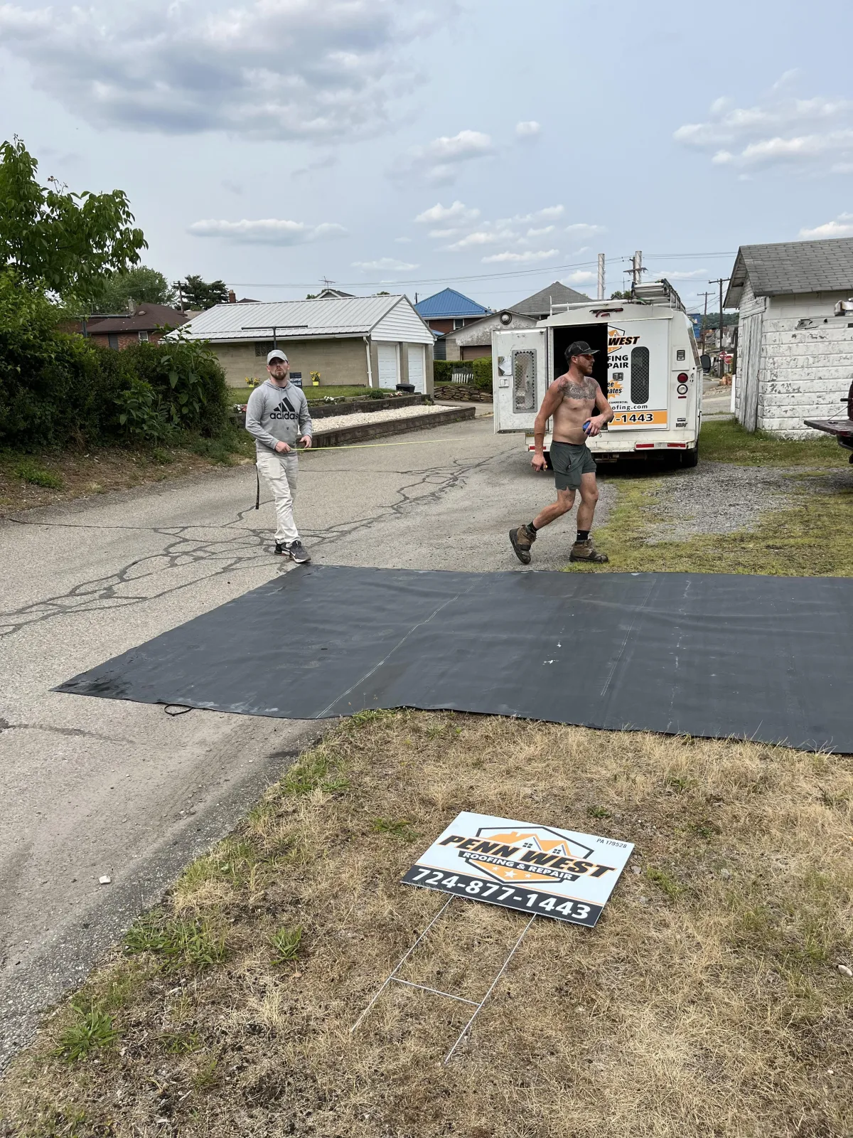 Penn West Roofing crew cutting rubber roofing membrane on the ground before flat roof installation in Brackenridge PA