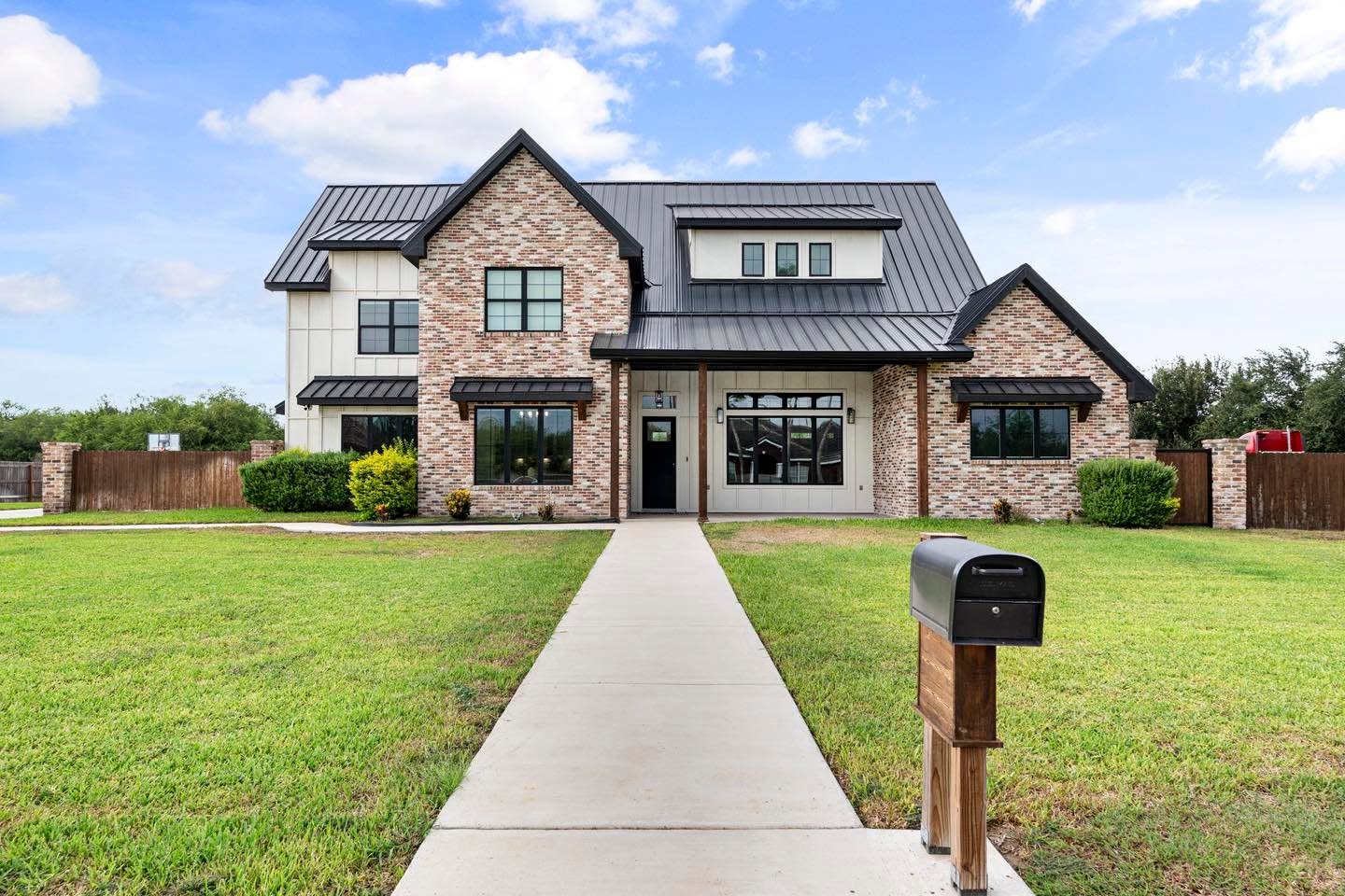 Brick modern farmhouse exterior with black metal roof, large windows, and covered front entry by South Texas Builders.